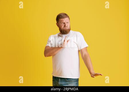 Homme barbu en t-shirt blanc montrant un geste de rejet sur fond de studio jaune. Dire non Banque D'Images