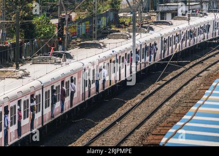 Un train plein de passagers en vitesse sur les voies devant des bâtiments à Mumbai, en Inde Banque D'Images