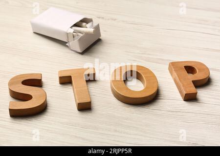 Paquet avec des cigarettes et le mot Stop fait de lettres sur la table en bois blanc. Concept non fumeur Banque D'Images