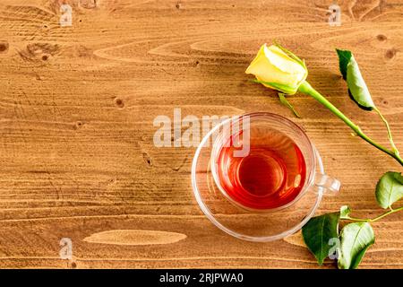 Une vue de dessus d'une rose jaune et une tasse de thé noir dans une tasse en verre transparent sur une table en bois. Banque D'Images