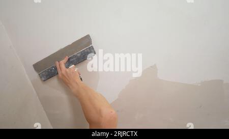 Poncer le plafond avant de peindre. Un ouvrier nettoie le plafond avec une spatule. Les mains des ouvriers réparent le plafond. Banque D'Images