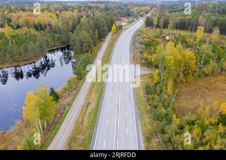 Une route panoramique serpentant à travers une végétation verdoyante, avec des arbres et des arbustes encadrant la route de chaque côté et un lac tranquille au loin Banque D'Images