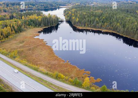 Une route panoramique serpentant à travers une végétation verdoyante, avec des arbres et des arbustes encadrant la route de chaque côté et un lac tranquille au loin Banque D'Images