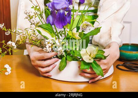 Une japonaise pratiquant l'ikebana. Les mains de la femme arrangent magnifiquement les fleurs dans un bol. Banque D'Images