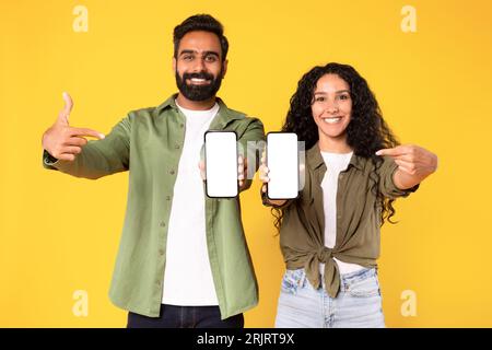 Couple du Moyen-Orient montrant deux écrans de téléphones cellulaires sur fond jaune Banque D'Images