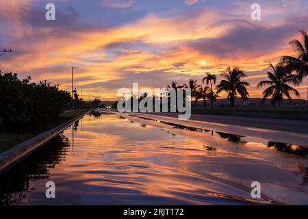 Une belle scène de route avec le ciel réfléchi sur la surface de l'eau au coucher du soleil. Banque D'Images