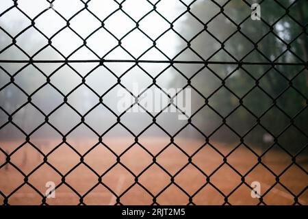 Tir horizontal sur un court de tennis vide dans la forêt dans le brouillard à travers une clôture. Le joueur de tennis frappe la balle sur le filet avec la raquette. Banque D'Images