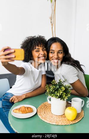 Deux copines heureux assis à table en prenant un selfies Banque D'Images