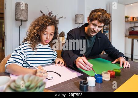Père et fille assis à la table dessinant et peignant ensemble Banque D'Images