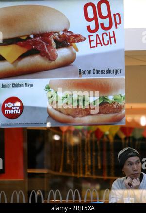Bildnummer : 51579535 Datum : 17.11.2006 Copyright : imago/Xinhua Kunde sitzt hinter einem Werbeplakat in einer Burger King-filiale in London - PUBLICATIONxNOTxINxCHN, Personen , Objekte ; 2006, London, Mann, Plakat, Werbung, Reklame, 99p chacun, cheeseburger au bacon, poulet Mayo junior, Schriftzug, BurgerKing, Fastfoodkette, restaurant, Schnellrestaurant, Restaurantkette, fastfood ; , hoch, Kbdig, Einzelbild, Gastronomie, Wirtschaft, Angleterre, , Banque D'Images