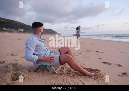 Femme courant vers le petit ami assis sur une chaise à la plage Banque D'Images