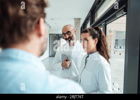 Médecins souriants parlant au patient dans le couloir Banque D'Images