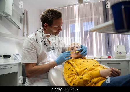 Dentiste souriant examinant les dents d'un garçon en clinique Banque D'Images