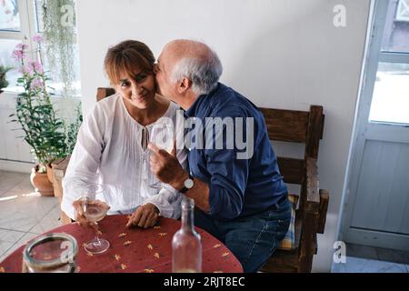 Heureux homme senior embrassant femme avec des verres de vin dans le café Banque D'Images