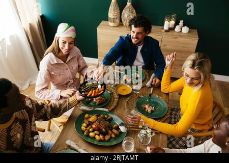 Amis souriants appréciant le déjeuner à la table à manger à la maison Banque D'Images