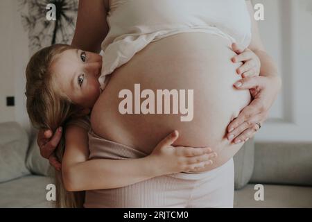 Fille embrassant la mère enceinte à la maison Banque D'Images