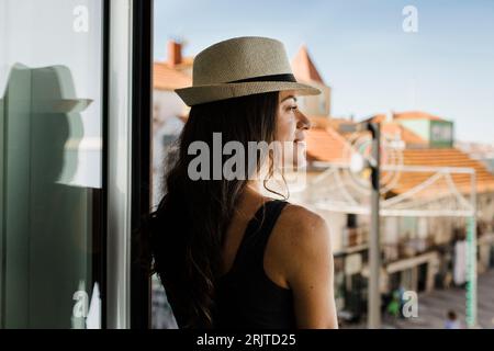 Jeune femme réfléchie portant un chapeau regardant par la fenêtre Banque D'Images