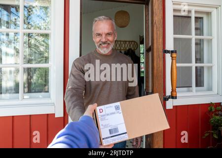 Homme souriant recevant le colis du livreur à la porte Banque D'Images