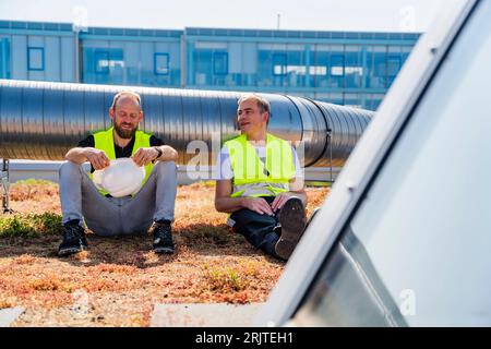 Deux techniciens portant des gilets réfléchissants font une pause sur le toit d’un bâtiment de l’entreprise Banque D'Images