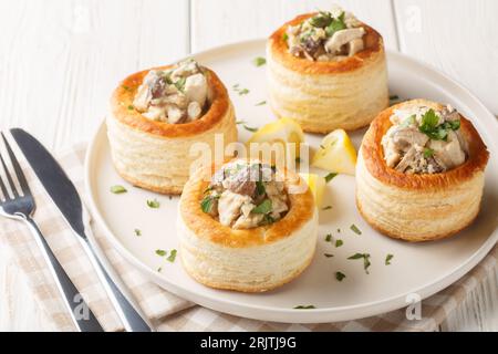 Vol-au-vent est un plat français fait de pâte feuilletée creuse avec un champignon de poulet crémeux remplissant closeup sur l'assiette sur la table en bois blanc. Horizo Banque D'Images