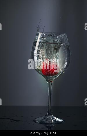 Les fraises tombaient dans un verre d'eau et éclaboussaient d'eau sur une table noire Banque D'Images