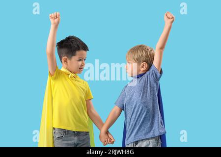 Mignons petits garçons avec capes de super-héros sur fond bleu Banque D'Images