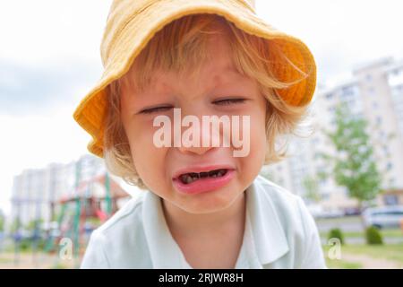 Un petit garçon triste dans un chapeau Panama jaune pleure dans la rue. Banque D'Images