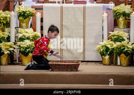 Un garçon dépose une contribution dans un panier pendant la messe sur l'autel d'une église catholique du sud de la Californie. Banque D'Images