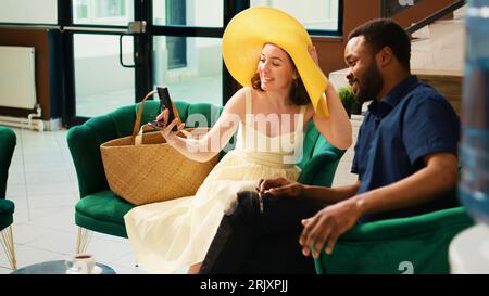 Les clients qui utilisent la salle de conférence vidéo dans le hall, discutent avec des amis après leur arrivée en voyage tropical de lune de miel. Diverses personnes appréciant le chat par vidéoconférence en ligne, salon de l'hôtel. Banque D'Images