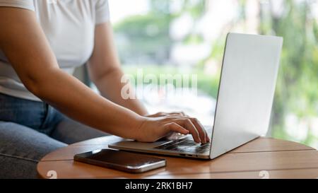 Image rapprochée d'une femme freelance travaillant à distance dans un café, utilisant son ordinateur portable pour gérer son travail à une table. Concept de style de vie urbain Banque D'Images