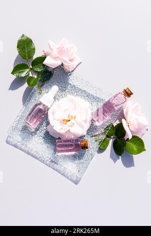 cosmetic product, oil, water based on rose petal oil in various bubbles on a glass square plate among the flowers of roses. natural care Stock Photo