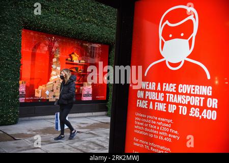 Photo du dossier datée du 19/11/2020 d'une femme portant un masque facial passant devant un écran conseillant le port de masques faciaux sur Oxford Street, Londres. Les mesures prises pendant la pandémie de Covid-19 telles que la distanciation sociale et le port de masques faciaux ont réduit «sans équivoque» la propagation des infections, a constaté un nouveau rapport. Date de publication : jeudi 24 août 2023. Banque D'Images