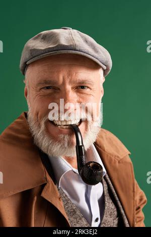 Portrait de détective confiant et positif portant un chapeau vintage, costume d'élégance avec tuyau dans la bouche sur fond de couleur verte. Banque D'Images