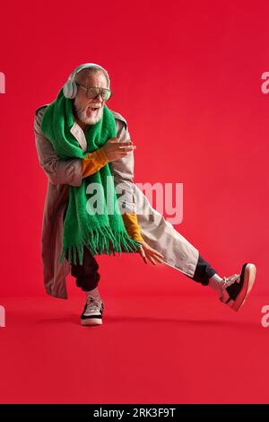 portrait en pied d'homme positif et drôle avec barbe dans une tenue lumineuse et décontractée avec des écouteurs qui danse et chante. Banque D'Images