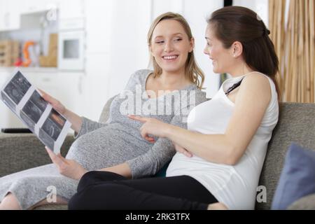 deux femmes enceintes regardant l'album photo d'échographie dans le salon Banque D'Images