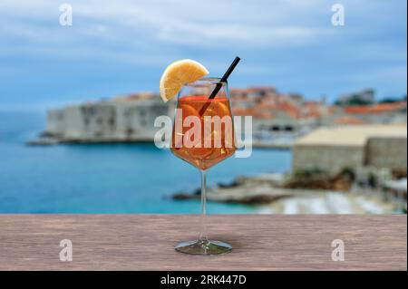 Cocktail spritz sur une table avec vue sur les murs de la forteresse de Dubrovnik, la plage et l'eau turquoise. Banque D'Images