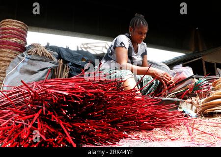 A woman processes a wine colored cane wood for weaving at Nigeria's largest cane 'village' at Mende in the Maryland District of Lagos. Cane craft in Nigeria, Africa's most populous country, is thriving amidst an economic downturn which has affected small scale businesses and people's earnings. At the village, dozens of people, including family members and the unemployed are engaged in weaving different household items like tables, baskets, wine carriers, flower pots with cane wood sourced from the swampy Niger Delta region. Lagos, Nigeria. Stock Photo