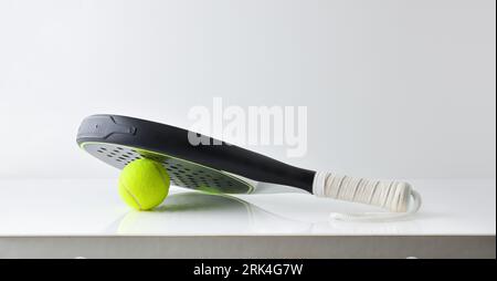 Deux raquettes de paddle-tennis noires et blanches reposant sur une balle réfléchie sur une table blanche et un fond blanc isolé. Vue avant. Banque D'Images