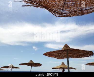 Parasols solaires sur la plage sur fond bleu ciel, papier peint de vacances d'été Banque D'Images