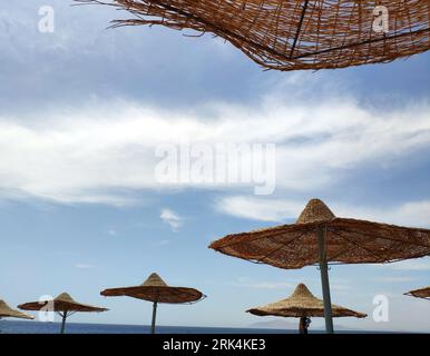 Parasols solaires sur la plage sur fond bleu ciel, papier peint de vacances d'été Banque D'Images