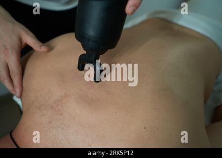Physiothérapeute expérimenté utilise un pistolet de massage sur le dos du client Banque D'Images