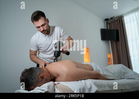 Physiothérapeute utilisant un masseur à percussion sur le haut du dos du patient Banque D'Images