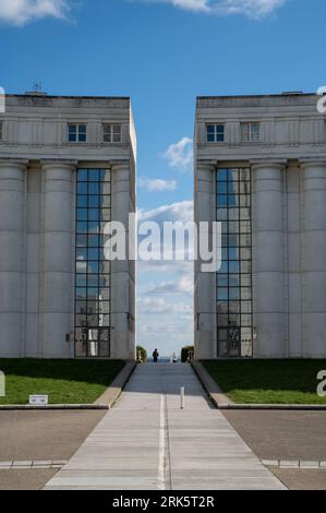 A symmetrical walkway between two modern office buildings, surrounded by lush greenery, leading to a clear blue sky Stock Photo