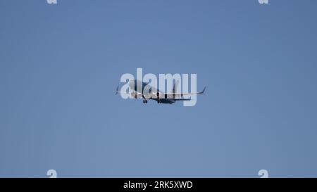 Un avion volant dans le ciel avec son train d'atterrissage étendu, planant sur un fond bleu de ciel Banque D'Images