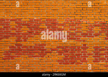 A close-up of a brick wall featuring a red painted clock mounted at the top Stock Photo