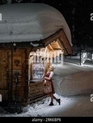 Une femme adulte se tient devant une cabane rustique en rondins dans la neige. Banque D'Images