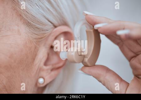 Main, gros plan et prothèse auditive dans l'oreille pour vieille femme, audio ou son pour l'écoute, les soins de santé ou la retraite. Dame senior, sourde ou personne avec Banque D'Images