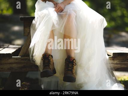 Une jeune femme assise sur un banc portant une robe de mariée blanche et des bottes brunes Banque D'Images