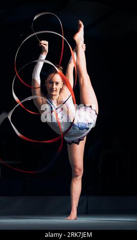 Femme, portrait et équilibre pour la gymnastique de ruban, la performance sportive ou la compétition dans l'arène de concert sombre. Athlète flexible, danseur et étirement Banque D'Images