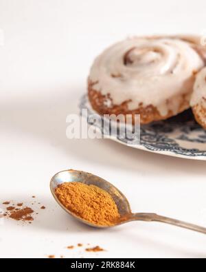 Une image en gros plan de deux rouleaux de cannelle Cinnabon sur des assiettes, avec une cuillère de cannelle en poudre sur le côté Banque D'Images